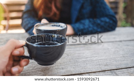 Close up image of two people clinking coffee mugs on wooden table 