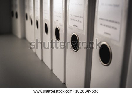a close up image of a typical paper and document management with row of white files and a tag label system storage on the office's steel shelves 
