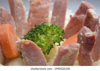 Close Up Image Of A Weird Dinner. A Ring Of Gammon Slices Embedded In Potato Mash Surround A Single Broccoli Floret And Two Carrot Pieces.