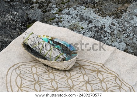 A close up image of a white sage smudge kit resting on a flower of life sacred geometry grid cloth. 