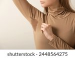 Close up image of woman in beige cotton turtleneck with sweat patch under armpit	