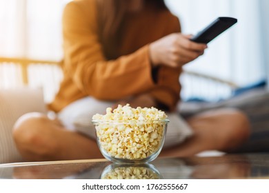 Close Up Image Of A Woman Eating Pop Corn And Searching Channel With Remote Control To Watch Tv While Sitting On Sofa At Home