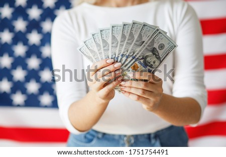 Close up image of woman hands with american dollars. Girl holding  money on American flag background. 
