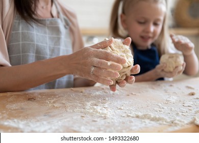 Close up image woman and little daughter knead dough with hands wooden table powdered with flour, small helper and mom preparing pastries or make pizza, cooking process and parent teach child concept