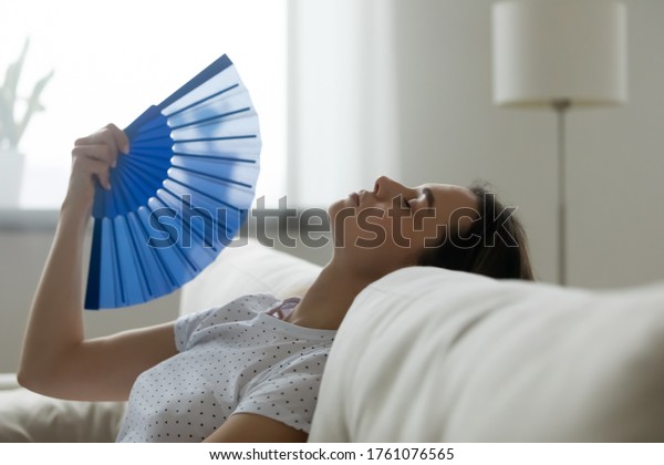 Close up image woman puts head on sofa cushions\
closed eyes feels sluggish due unbearable heat, waves hand blue fan\
cool herself, hot summer flat without air-conditioner climate\
control system concept
