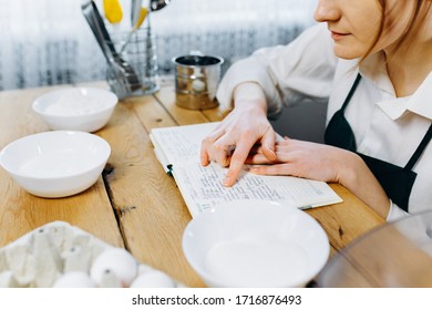 Close Up Image Of Woman Sitting At Wooden Kitchen Table Looking To  Recipe Book And Trying To Choose What To Cook. Cooking At Home Concept, Lifestyle. Ketogenic Diet And Menu