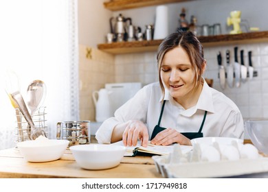 Close Up Image Of Woman Sitting At Wooden Kitchen Table Looking To  Recipe Book And Trying To Choose What To Cook. Cooking At Home Concept, Lifestyle. Ketogenic Diet And Menu