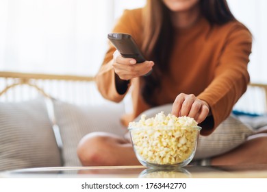 Close Up Image Of A Young Woman Eating Pop Corn And Searching Channel With Remote Control To Watch Tv While Sitting On Sofa At Home