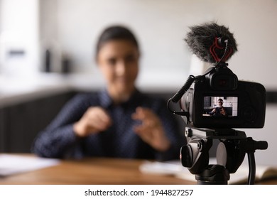 Close up Indian blogger using professional digital camera, recording video, tutorial or vlog, sitting at work desk, young woman teacher business coach shooting webinar, speaking, explaining,