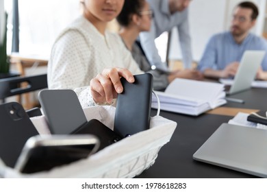 Close up Indian businesswoman putting phone in basket, employee entrepreneur woman sitting at table in boardroom, involved in briefing, meeting, no cellphone zone in office or digital detox concept