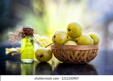 Close up of Indian gooseberry with its extracted essence or concentration in a transparent bottle on wooden surface with raw amla in a fruit and vegetable basket.