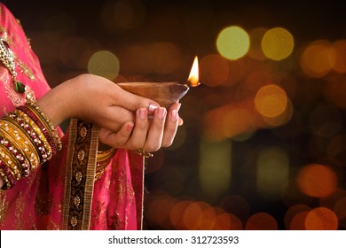 Close up Indian woman in traditional sari lighting oil lamp and celebrating Diwali or deepavali, fesitval of lights at temple. Female hands holding oil lamp, beautiful lights bokeh background.