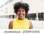 Close up individual portrait of one teenage african american girl smiling and looking at camera outside. A young adult woman staring front and laughing. Afro female gazing with friendly expression