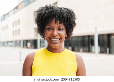 Close up individual portrait of one teenage african american girl smiling and looking at camera outside. A young adult woman staring front and laughing. Afro female gazing with friendly expression - Powered by Shutterstock