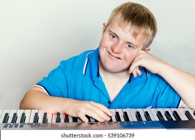 Close up indoor studio portrait of young pianist with down syndrome next to piano keyboard.