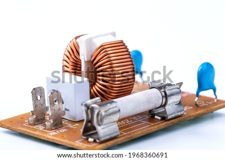 Close up of induction coil with copper wire winding soldered on printed circuit board and electric fuse isolated on white, toroidal inductor. Selective focus.