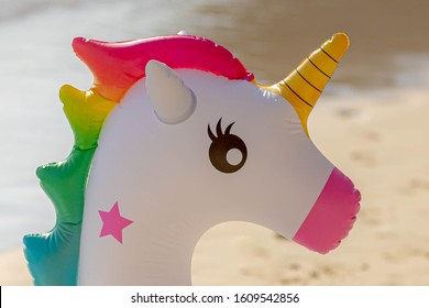 Close Up Of Inflatable Unicorn With White And Rainbow Color On The White Sand Beach, Selective Focus Of Colourful Swim Ring Or Inner Tube.