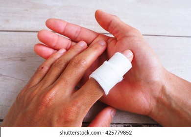 Close up of injured finger with white medicine bandage on wooden background