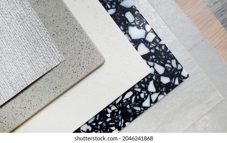 close up interior construction material samples containing grey fabric wallpaper, grainy artificial stone, black terrazzo stone, travertine tile, wooden laminate (focus at stone texture).