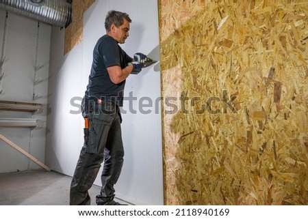 Close up of interior partition of work building. Man is screwing drywall to wood wall with cordless screwdriver. Construction concept. Sweden.