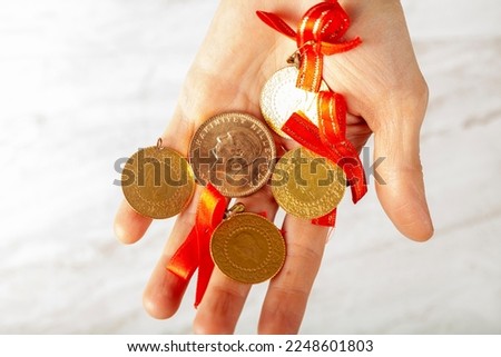 Close up isolated image of assorted sizes of Turkish gold coins including cumhuriyet, yarim and ceyrek in a white woman's hand . Some are attached to red ribbons for giving as gifts in weddings.