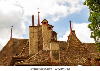 Close Up Isolated Image Of A Complex Traditional Roof Structure On A Historic Swiss Building. Hexagonal Clay Tiles Cover The Steep Slope Of The Roof With Chimneys And Wind Roses In Between.