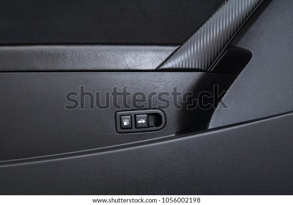 Close up isolated image of the plastic gas (petrol)\
tank lid opening button as well as the trunk (boot) opening button\
next to a pleather armrest with a carbon fiber vinyl door panel\
grip.
