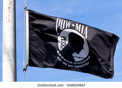 Close up isolated image of a POW, MIA (Prisoner of War, Missed in Action) Flag flying in the wind on a sunny day. Emblem depicts silhouette of a prisoner with barbed wire and guard tower in background - Powered by Shutterstock