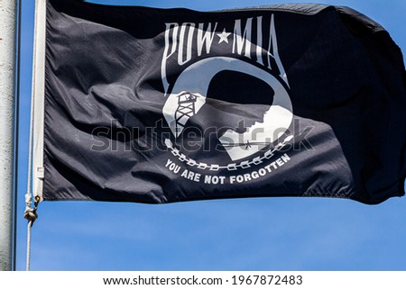 Close up isolated image of a POW, MIA (Prisoner of War, Missed in Action) Flag flying in the wind on a sunny day. Emblem depicts silhouette of a prisoner with barbed wire and guard tower in background