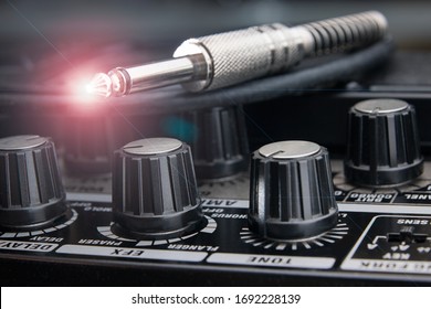 Close Up Of A Jack Plug For Electric Guitar Resting On The Panel Of An Amplifier With Detail Of The Valves For The Various Adjustments And Light Effect On The Tip Of The Plug