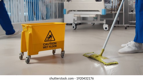 Close Up Of Janitor Washing Floor With Mop And Bucket In Hospital Ward. Cropped Shot Of Nurse Or Cleaning Staff Mopping Floor In Clinic. Healthcare And Hygiene Concept