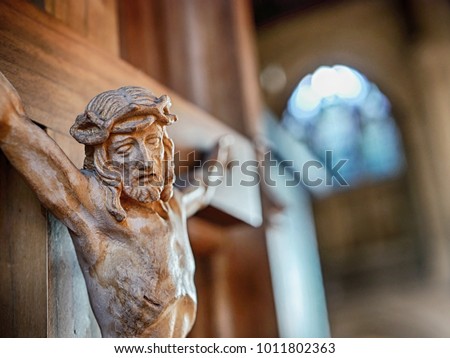 Close up of Jesus' face and crown of thorns on a wooden crucifix with church and stained glass windows in the background