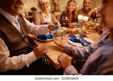 Close Up Of Jewish Boy Receiving Hanukkah Gelt From His Grandfather During Family Meal At Dining Table. 