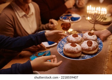 Close up of Jewish family having Hanukkah sufganiyah donuts for dessert at dining table.