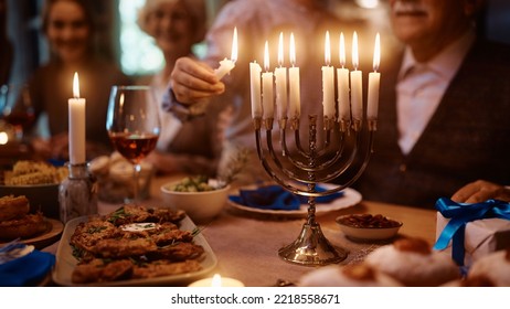 Close Up Of Jewish Kid Lighting The Menorah During Family Dinner On Hanukkah.