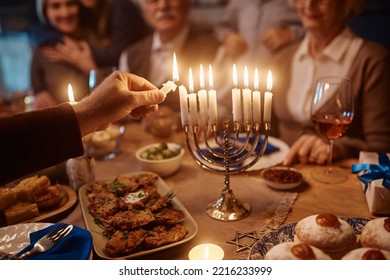 Close Up Of Jewish Man Lighting The Menorah During Family Dinner On Hanukkah.