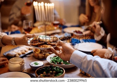 Close up of Jewish people passing latkes during traditional Hanukkah dinner at dining table.