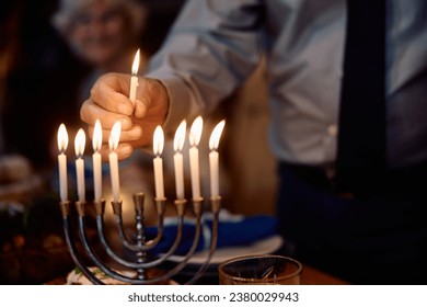 Close up of Jewish senior man lights candles in menorah during Hannukah celebration at home. 