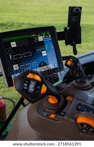 Close up of a John Deere tractor console shows dual joysticks, lit buttons, and a large touchscreen with rows guidance and hydraulic icons, indicating automated steering.