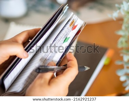 Close up of journal with colorful tags for organization and planning. Woman hands holding a notebook with pen for writing and studying with stickers for label notes. Office and school supplies