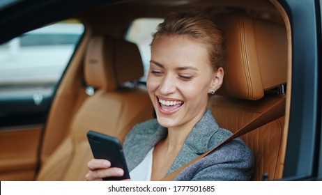 Close Up Joyful Business Woman Using Smartphone At Luxury Car. Happy Businesswoman Reading Sms On Mobile Phone At Car. Portrait Of Cheerful Woman Looking Phone Behind Steering Wheel.