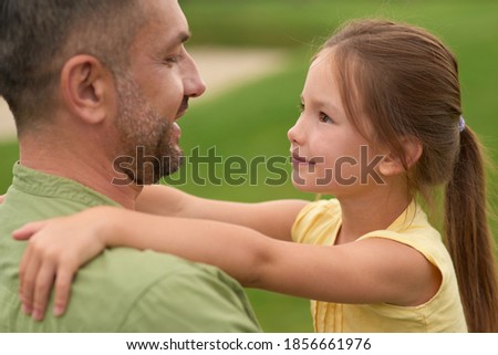 Close up of joyful little girl looking at her happy dad, hugging him while spending time together outdoors on a warm day