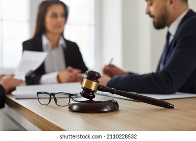 Close up of a judge's gavel and glasses on a wooden table, and an experienced lawyer meeting with a group of clients and giving a consultation in the background. Law services, legal advice concept