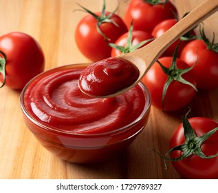 Close up of ketchup and tomatoes placed on a wooden background. Scoop ketchup with a spoon.