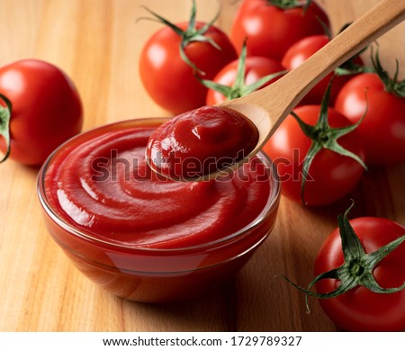 Close up of ketchup and tomatoes placed on a wooden background. Scoop ketchup with a spoon.