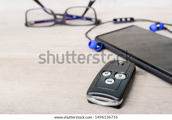 Close up key\
of car Smart phone and bluetooth headset,glasses on wood floor\
holiday equipment concept for touring\
