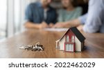 Close up of key and tiny toy house on table. Married couple buying house, consulting, lawyer, legal advisor, real estate agent, bank manager, signing mortgage agreement in background