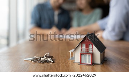 Close up of key and tiny toy house on table. Married couple buying house, consulting, lawyer, legal advisor, real estate agent, bank manager, signing mortgage agreement in background