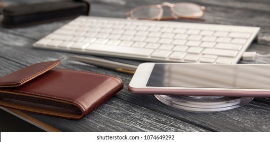 Close up with a keyboard, a men's purse, spectacles and a wireless charger for mobile devices. A nice and simple layout.