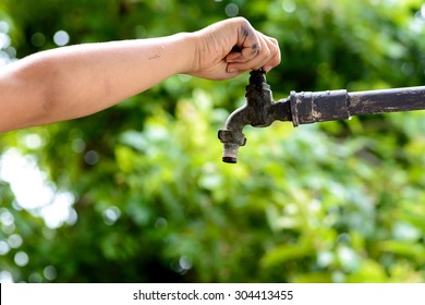 Close up kid hand open for water drop from old grunge brass faucet on green bokeh from tree background. Water shortage and earth day concept.